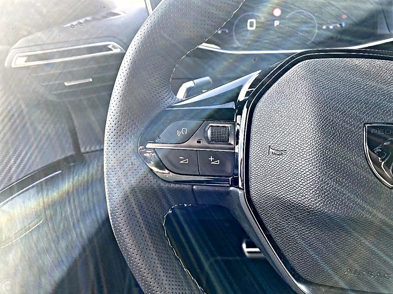 Gros plan sur le volant cuir perforé noir du Peugeot 2008 1.2 hybrid 145 GT avec commandes intégrées et tableau de bord numérique.