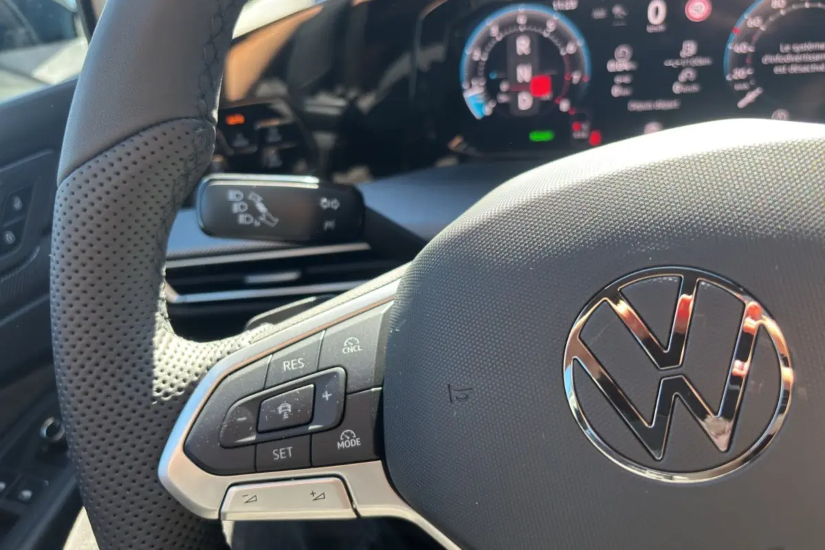 Gros plan sur le volant cuir multifonctions de la Volkswagen Golf TDI 150 R-Line 2026 avec affichage numérique en arrière-plan.