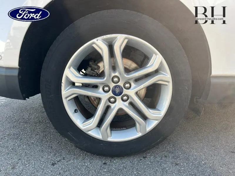 Gros plan sur la roue avant droite avec jante alliage argentée du Ford Edge blanc Platinum de 2016.