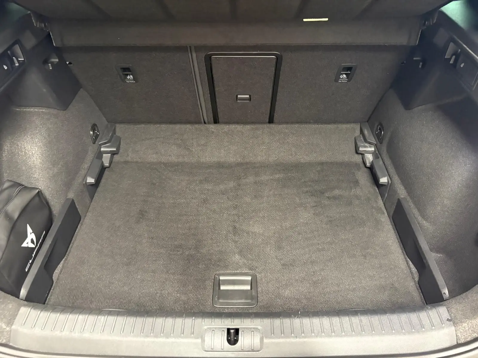 Coffre spacieux du CUPRA Formentor gris magnétique vu de l'arrière, avec tapis de sol et rangement latéral marqué Cupra.