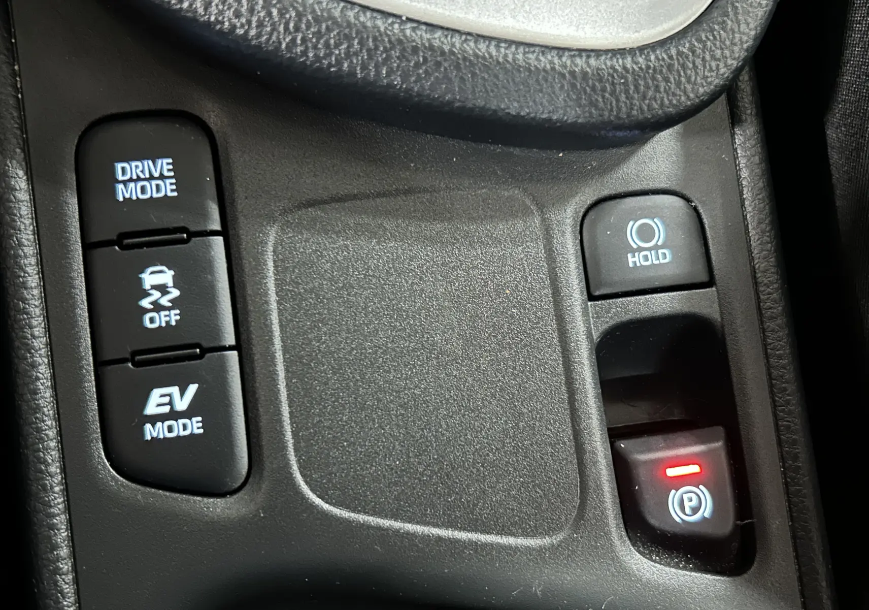 Gros plan sur les commandes de mode de conduite et frein à main électronique dans une Toyota Yaris Cross gris minéral.