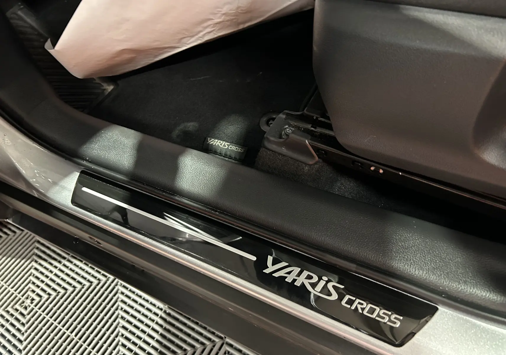 Gros plan intérieur sur la plaque de seuil de porte noire avec logo Yaris Cross sur un Toyota gris minéral.