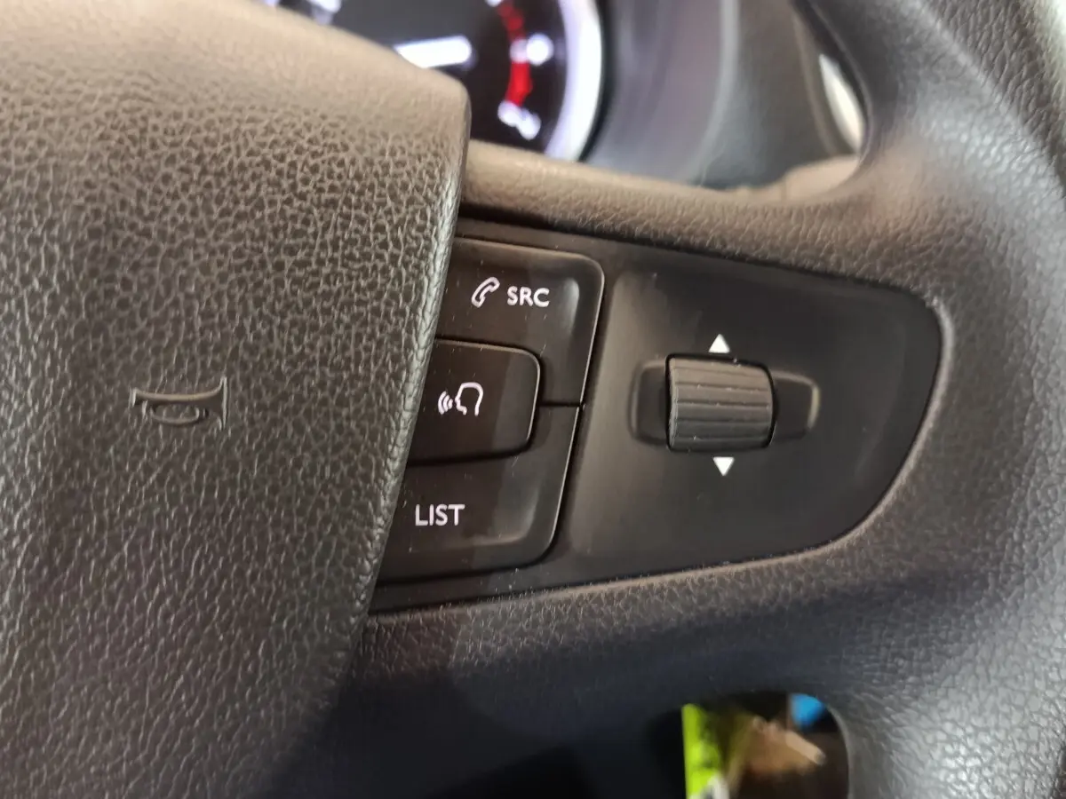 Gros plan sur les commandes noires du volant du Peugeot Expert Fourgon blanc, avec boutons SRC et liste visibles.