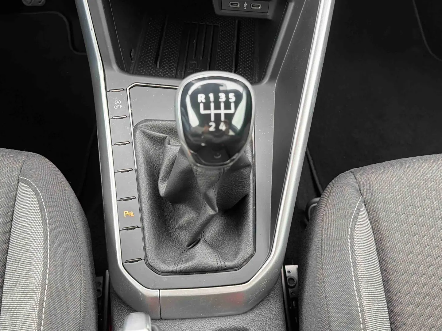 Vue rapprochée du levier de vitesses manuel noir entouré des sièges tissu gris dans une Volkswagen Polo 2025.