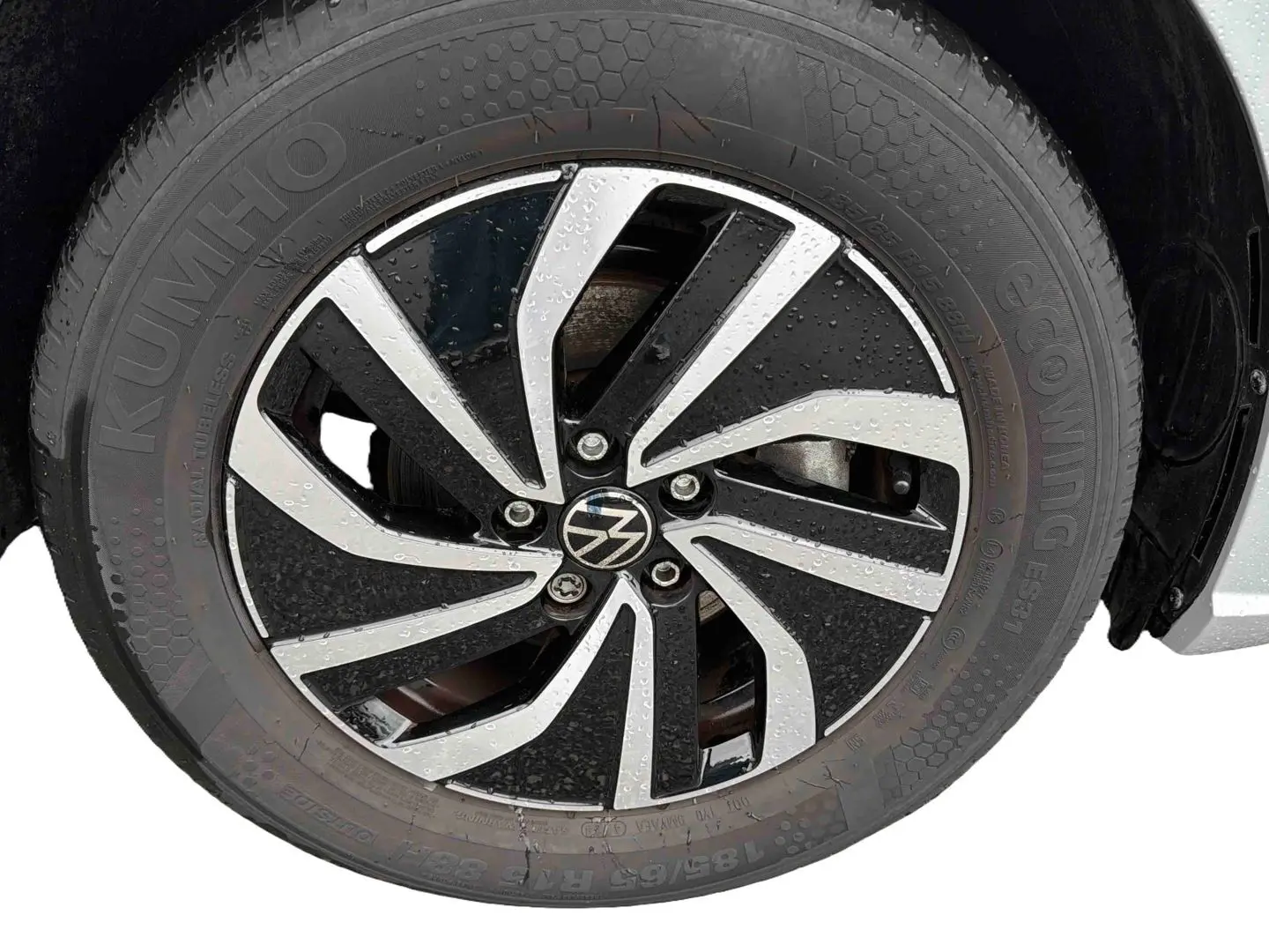 Gros plan sur la jante alliage 15 pouces bicolore avec logo Volkswagen sur pneu Kumho, véhicule gris visible en arrière-plan.