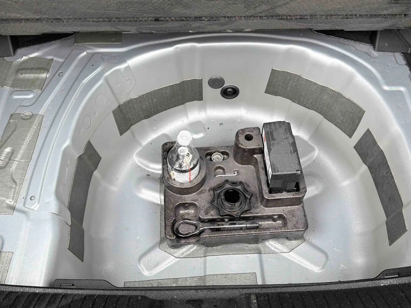 Vue plongeante sur le coffre ouvert d'une Volkswagen Polo grise, montrant le logement de la roue de secours vide avec outils.