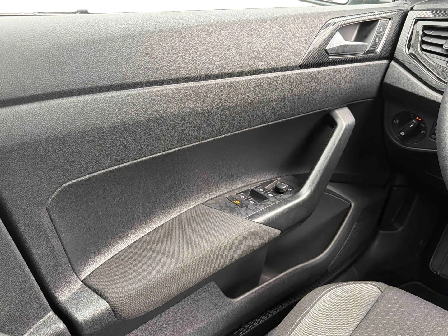 Vue intérieure côté gauche de la porte conducteur grise de la Volkswagen Polo 2025 avec commandes de vitres et tissu noir.
