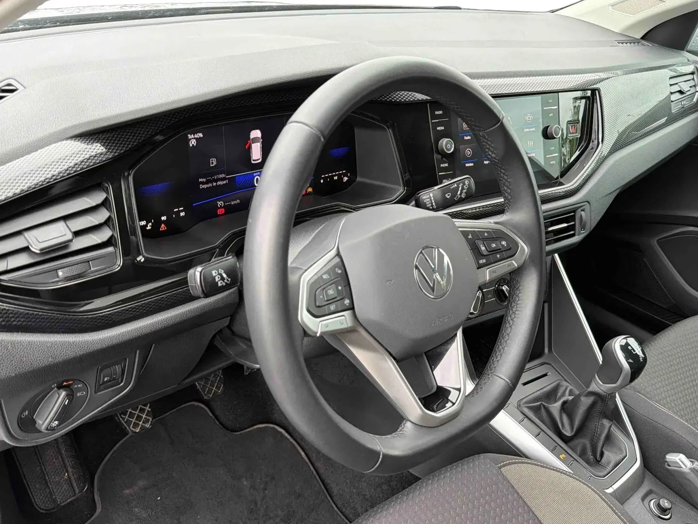 Vue intérieure du poste de conduite de la Volkswagen Polo grise, avec volant multifonctions et levier de vitesse manuel visible.