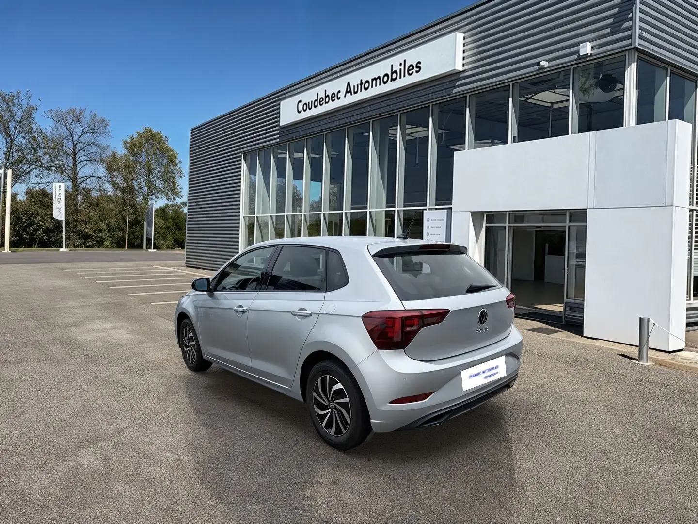 Volkswagen Polo grise vue 3/4 arrière droit, avec vitres surteintées et jantes alliage 15 pouces devant un concessionnaire.