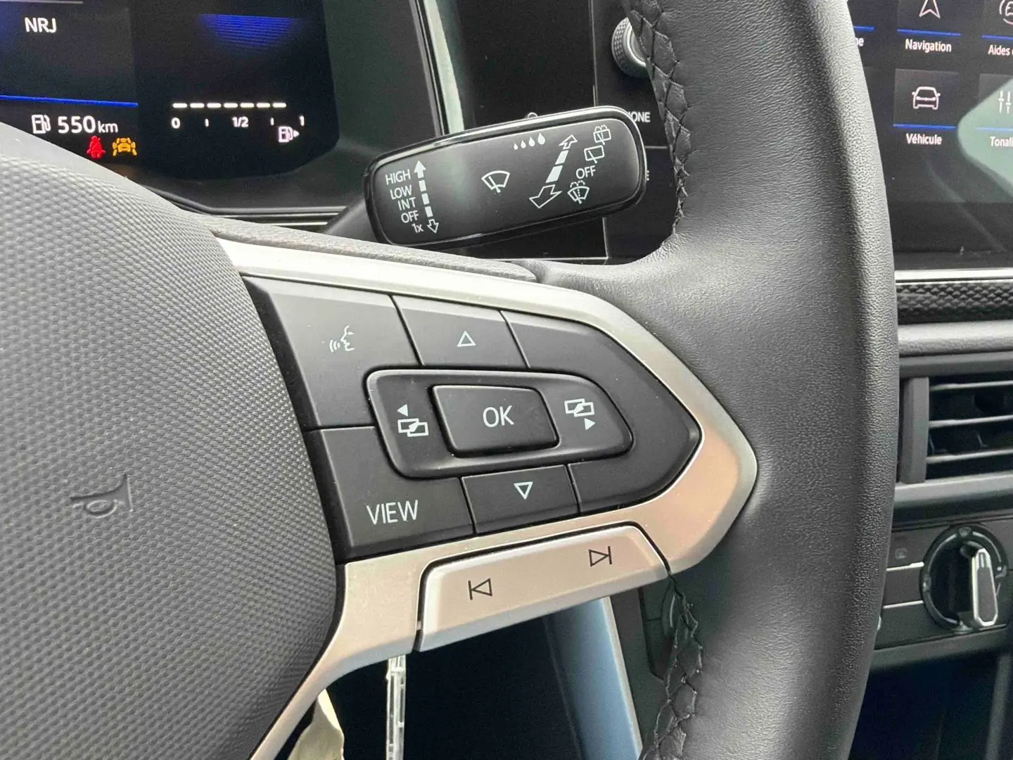 Gros plan sur les commandes gauche du volant noir de la Volkswagen Polo 2025 avec affichage digital en arrière-plan.