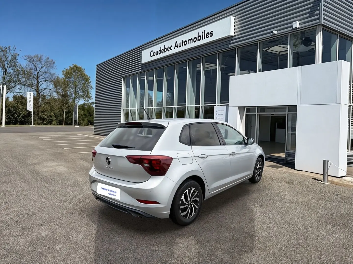 Volkswagen Polo grise vue 3/4 arrière droit, stationnée devant un bâtiment commercial moderne.