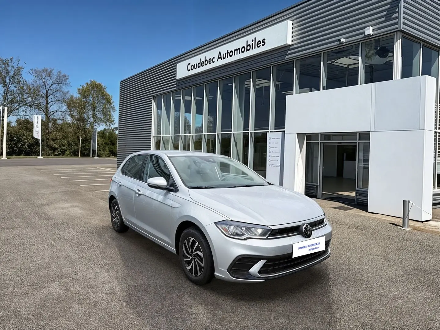 Volkswagen Polo grise vue 3/4 avant droit devant un bâtiment de concession automobile.