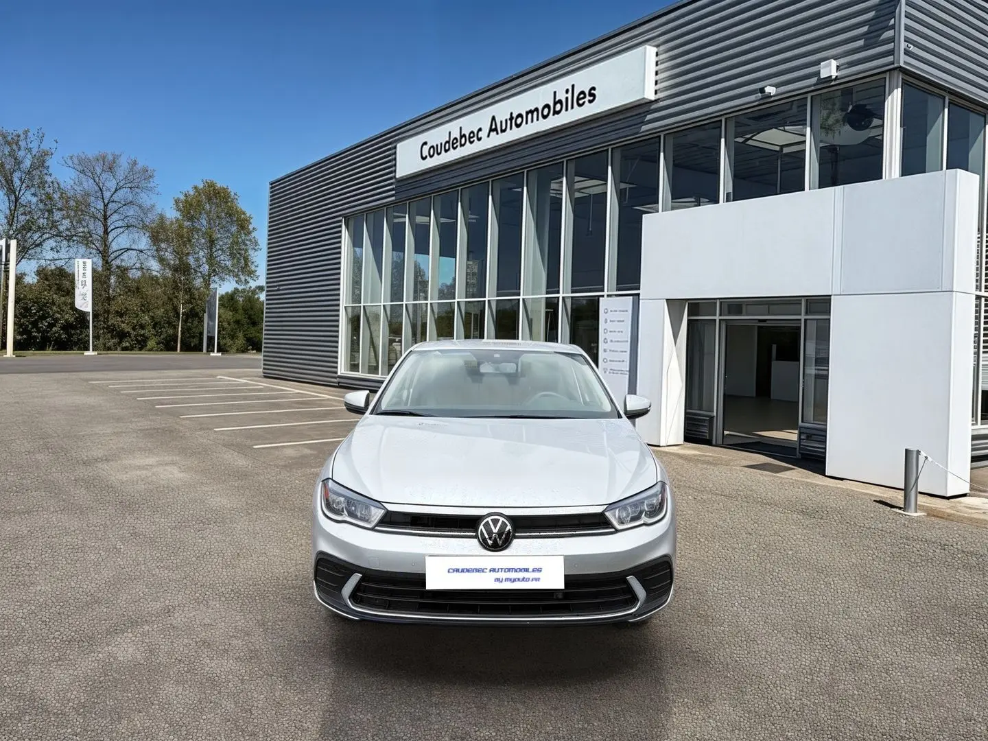 Vue avant d'une Volkswagen Polo grise 2025 stationnée devant un bâtiment moderne de concession automobile.
