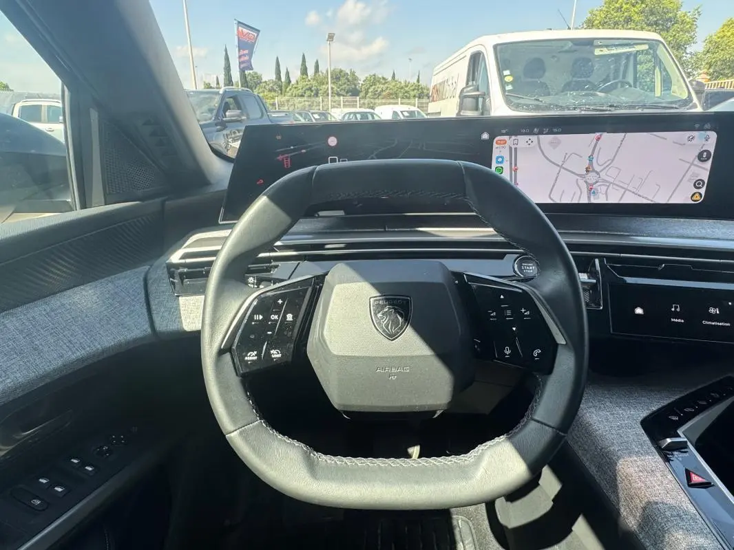 Vue intérieure centrée sur le volant compact du Peugeot 3008 Hybrid 2025 avec cockpit numérique et finition tissu gris.
