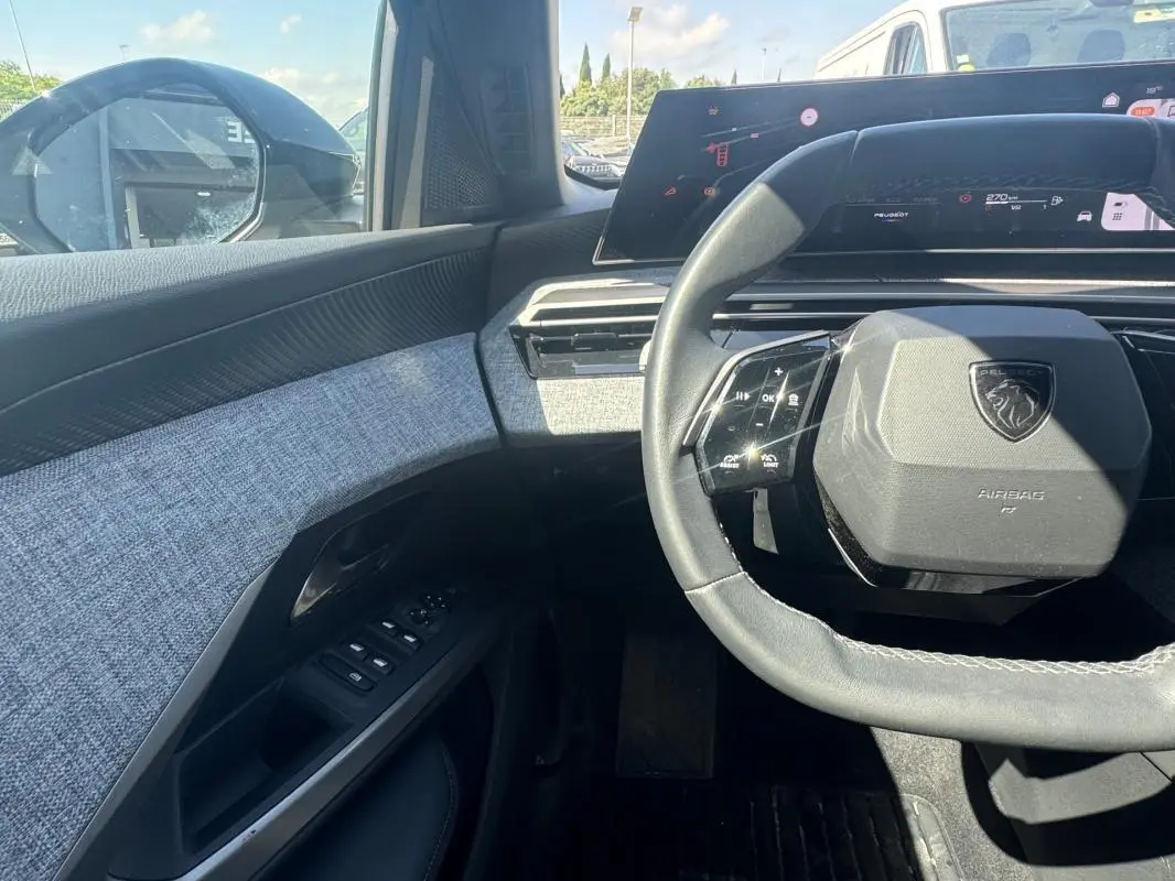 Vue intérieure côté conducteur du Peugeot 3008 Hybrid 2025, volant compact et tableau de bord numérique avec finition tissu gris.
