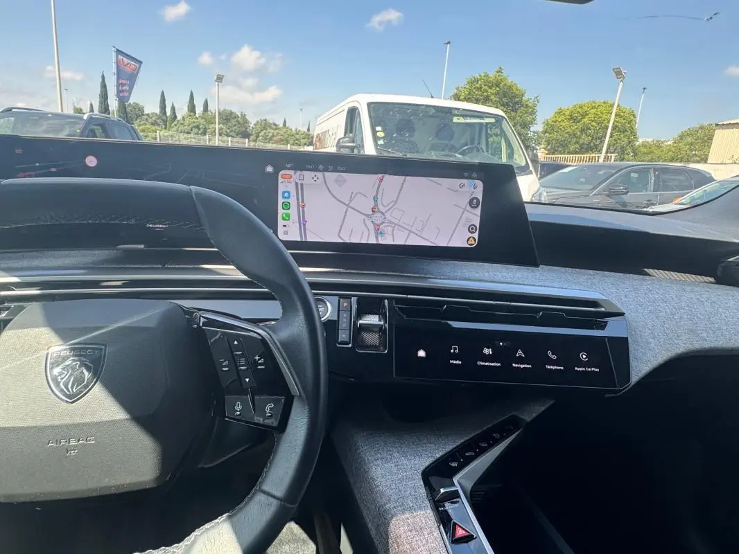 Vue intérieure du tableau de bord du Peugeot 3008 Hybrid 2025, avec volant noir et écran tactile central affichant la navigation.