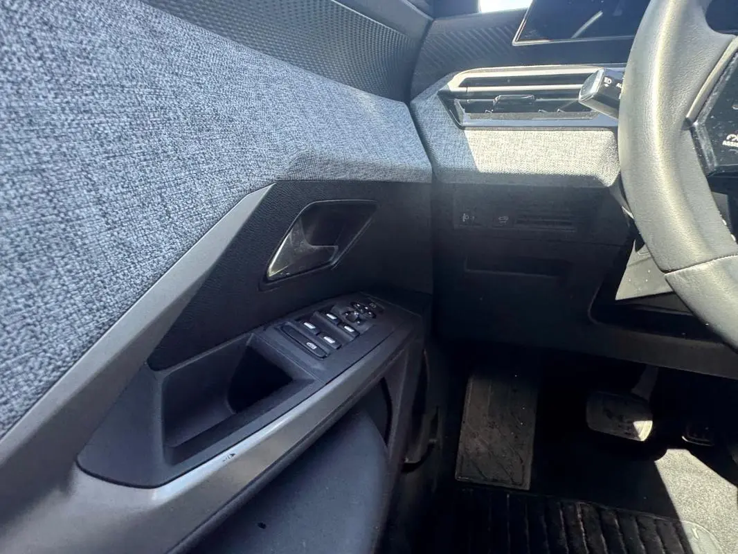 Vue intérieure côté gauche du Peugeot 3008 Hybrid 136 e-DCS6 Allure 2025, montrant la portière avec commandes et tissu gris.