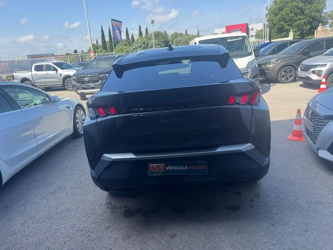 Vue arrière d’un Peugeot 3008 Hybrid gris foncé avec feux arrière allumés, garé parmi d’autres véhicules.