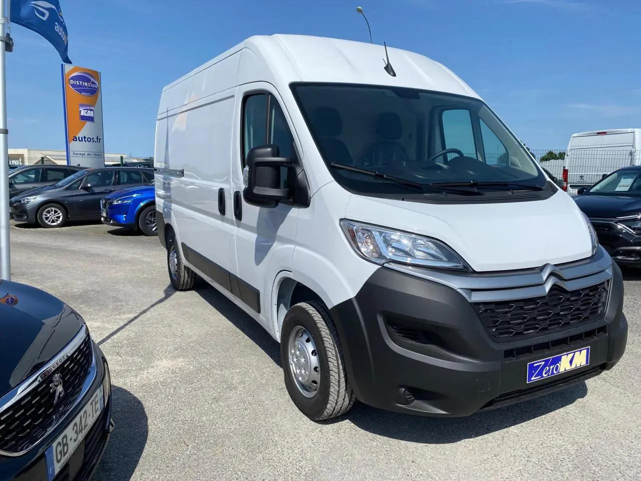 Vue 3/4 avant d'un utilitaire Citroën Jumper blanc avec pare-chocs noirs et rétroviseurs noirs sur parking.
