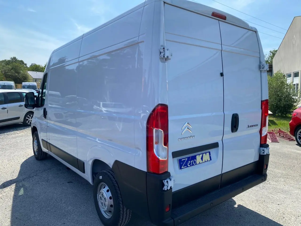Vue 3/4 arrière droite d'un Citroën Jumper blanc 2023 avec portes arrière tôlées et plaque Zéro KM visible.