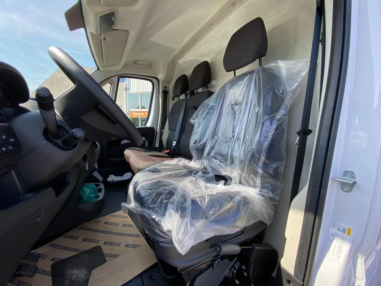 Vue intérieure côté conducteur du Citroën Jumper 2023, sièges avant en tissu avec protection plastique.