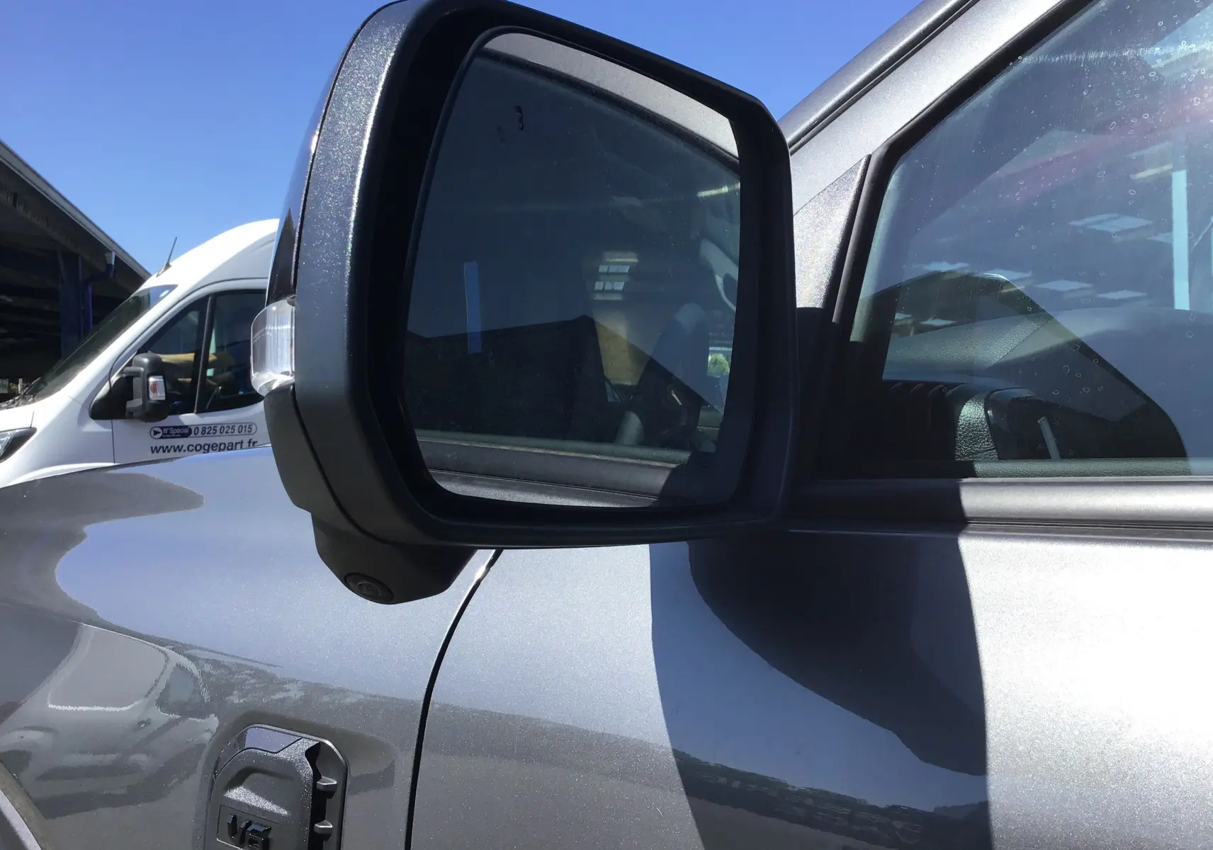 Rétroviseur côté gauche du Ford Ranger Double Cabine gris carbone, avec reflet de l'habitacle et caméra intégrée.