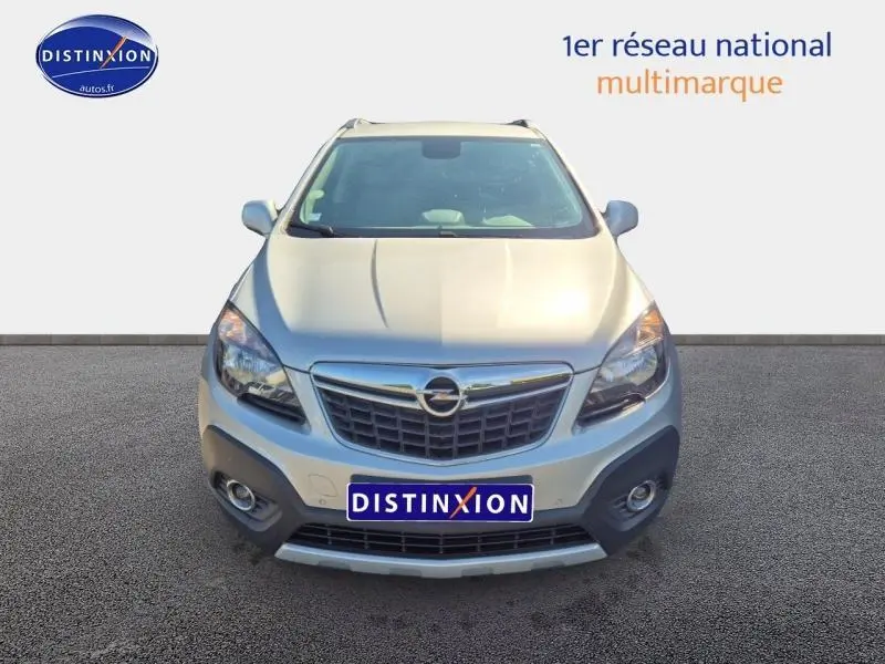 Vue avant d'un Opel Mokka gris astéroïde 2016 avec calandre chromée et phares halogènes allumés.