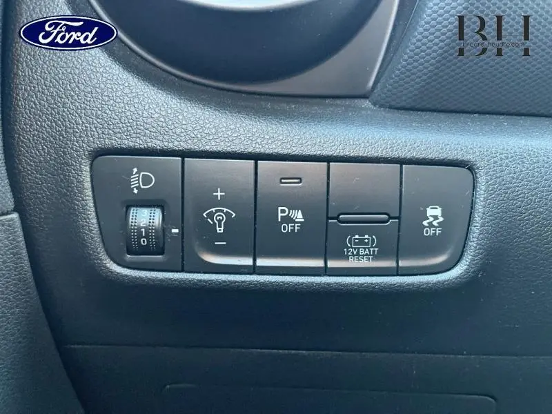 Gros plan sur les commandes noires du tableau de bord d’un Hyundai Kona 2022, boutons d’assistance et réglages lumineux.