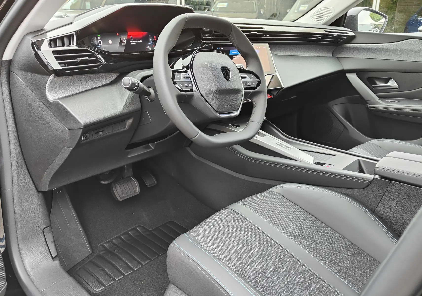 Vue intérieure côté conducteur de la Peugeot 308 PureTech 130 Allure Pack 2023, tableau de bord moderne et sièges gris.