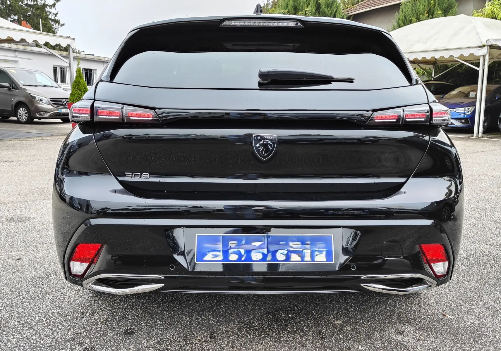 Vue arrière d'une Peugeot 308 PureTech 130 Allure Pack noire de 2023 avec feux LED et double sortie d'échappement chromée.