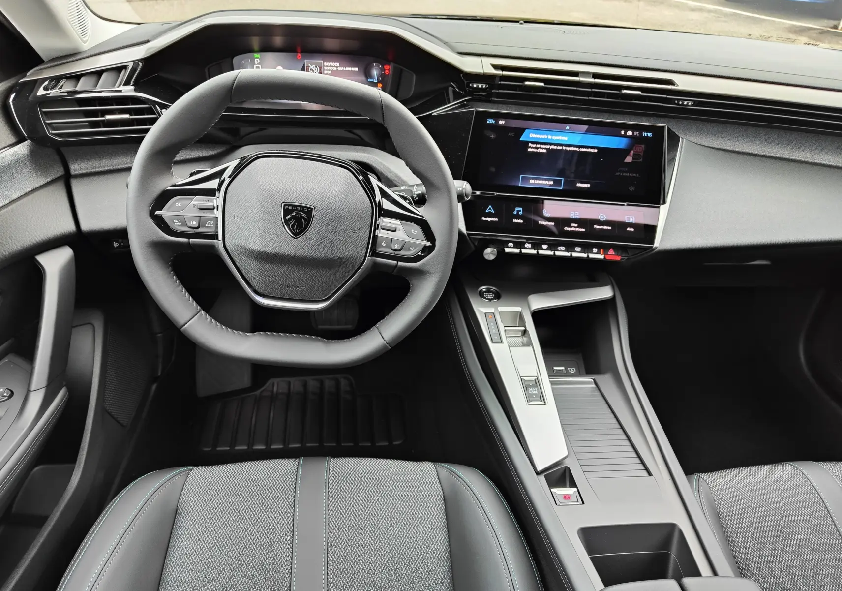 Vue intérieure avant de la Peugeot 308 PureTech 130 Allure Pack 2023 noire, tableau de bord et volant compact multifonction.