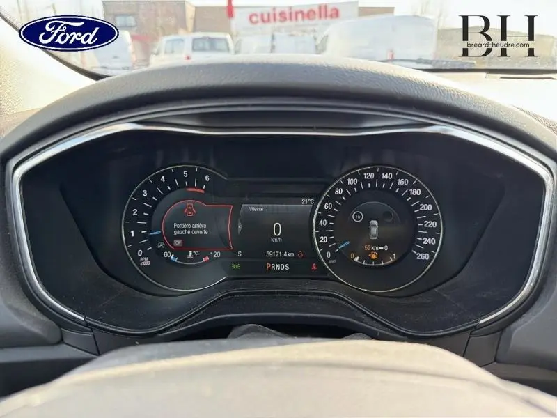 Vue rapprochée du tableau de bord numérique de la Ford Mondeo gris Premium, affichant la vitesse à 0 km/h et une porte arrière ouverte.