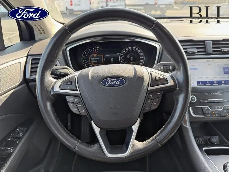 Vue intérieure centrée sur le volant cuir multifonction de la Ford Mondeo 2021 avec tableau de bord et écran tactile visibles.