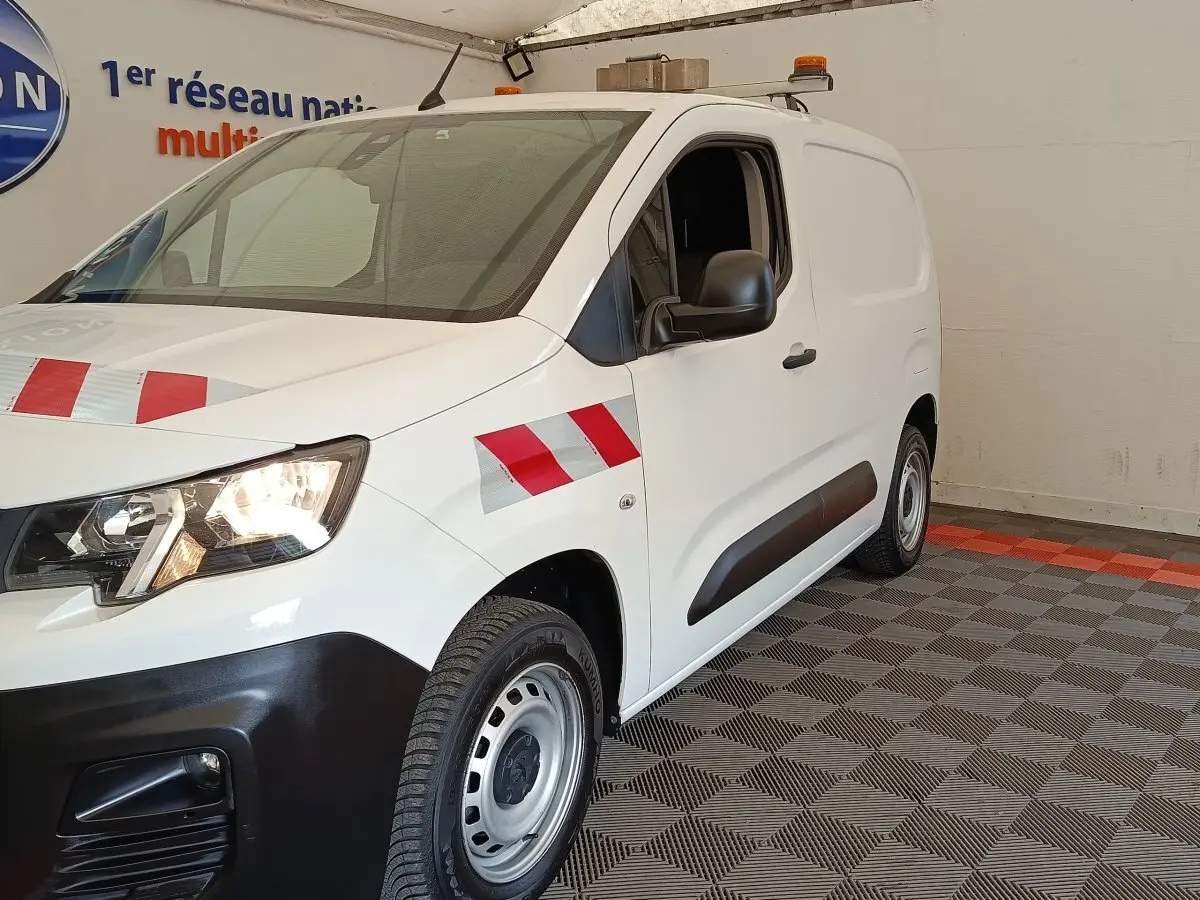 Vue 3/4 avant droite d’un Peugeot Partner blanc avec bandes réfléchissantes rouges et grises sur l’aile et le capot.