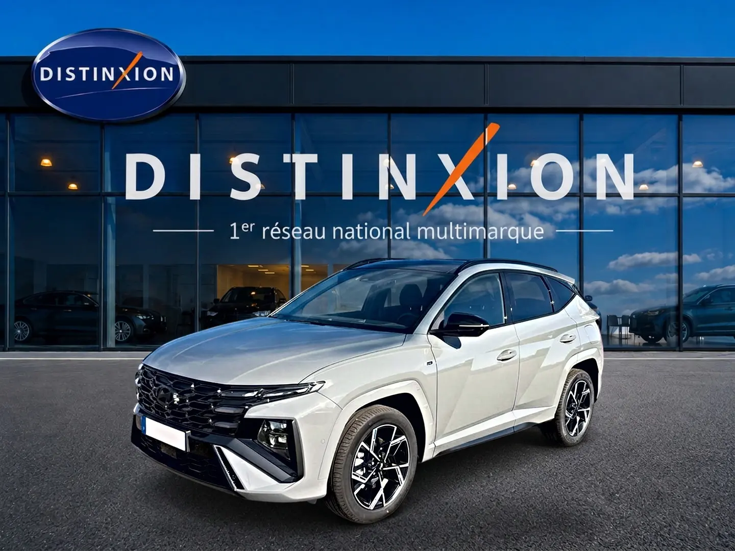 Vue 3/4 avant droite d'un Hyundai Tucson gris shadow avec calandre noire et jantes alu noires devant un showroom Distinxion.