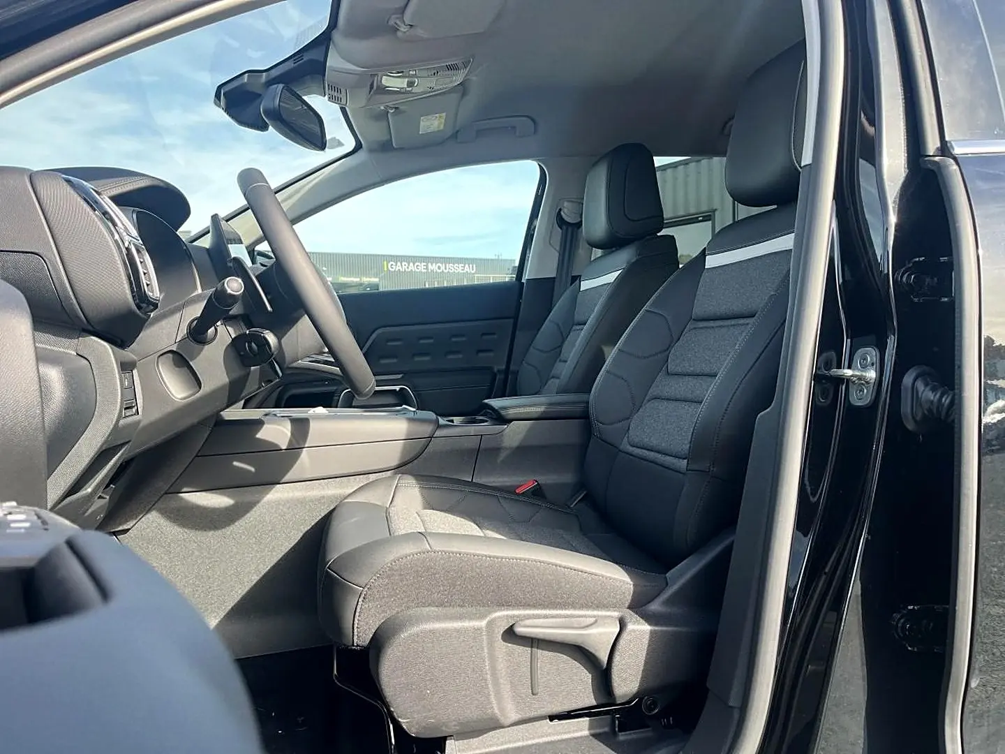 Vue intérieure côté conducteur du Citroën C5 Aircross noir 2025, sièges tissu et cuir noir avec console centrale visible.