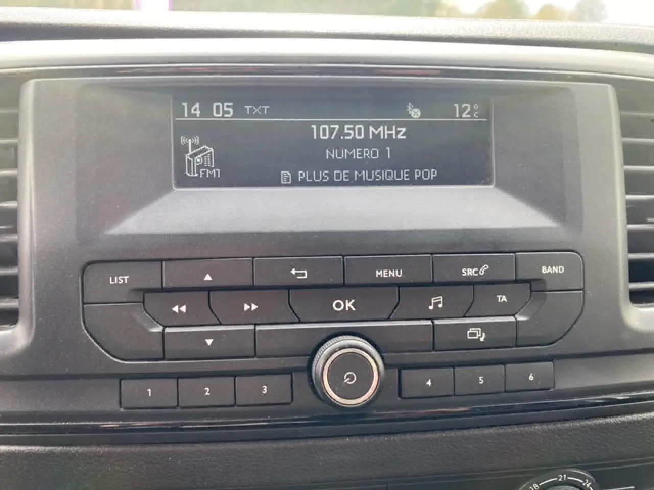 Gros plan sur l'autoradio du Citroën Jumpy blanc 2019 affichant la fréquence 107.50 MHz et la température extérieure 12°C.