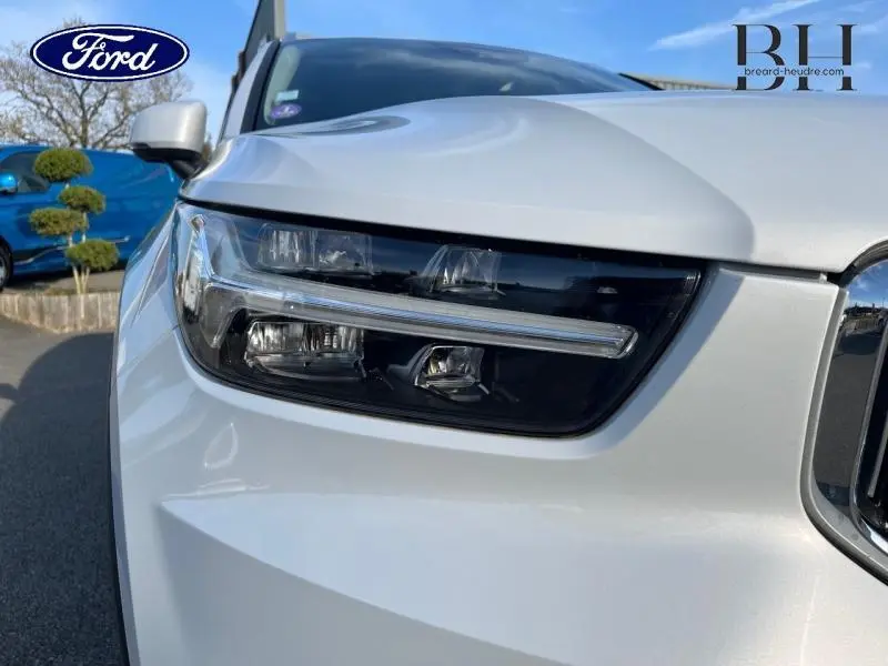 Gros plan sur le phare avant gauche du Volvo XC40 gris Glacier, mettant en valeur la signature lumineuse LED distinctive.