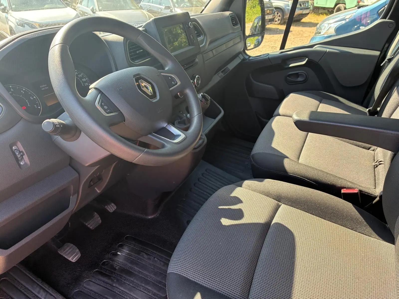Vue intérieure côté conducteur du Renault Master gris 2023, montrant le volant, la console centrale et les sièges tissu noirs.