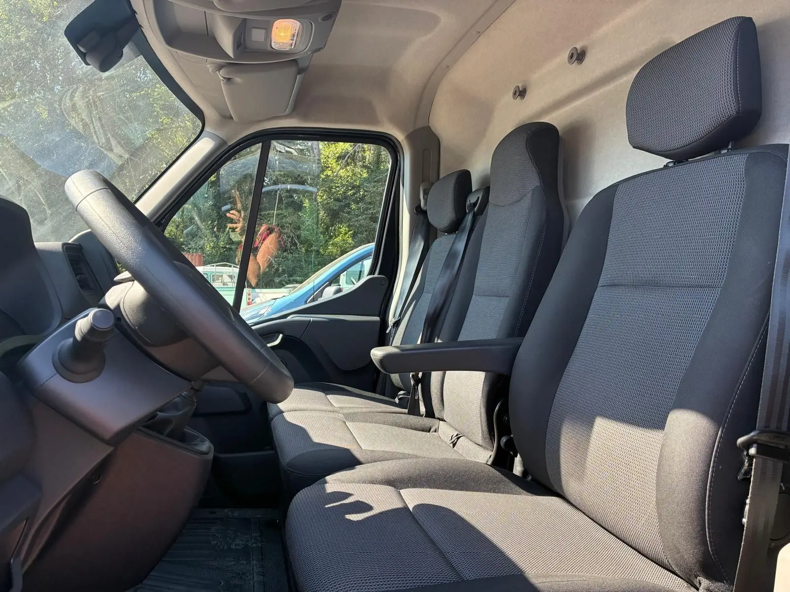 Vue intérieure côté conducteur du Renault Master 2023, sièges tissu gris avec accoudoir et volant visible.