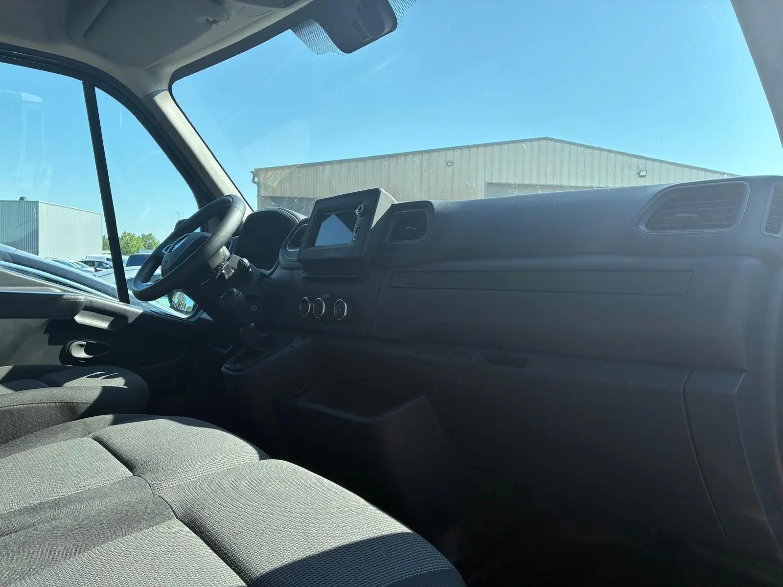 Vue intérieure côté conducteur du tableau de bord et des sièges en tissu gris du Renault Master 2023.
