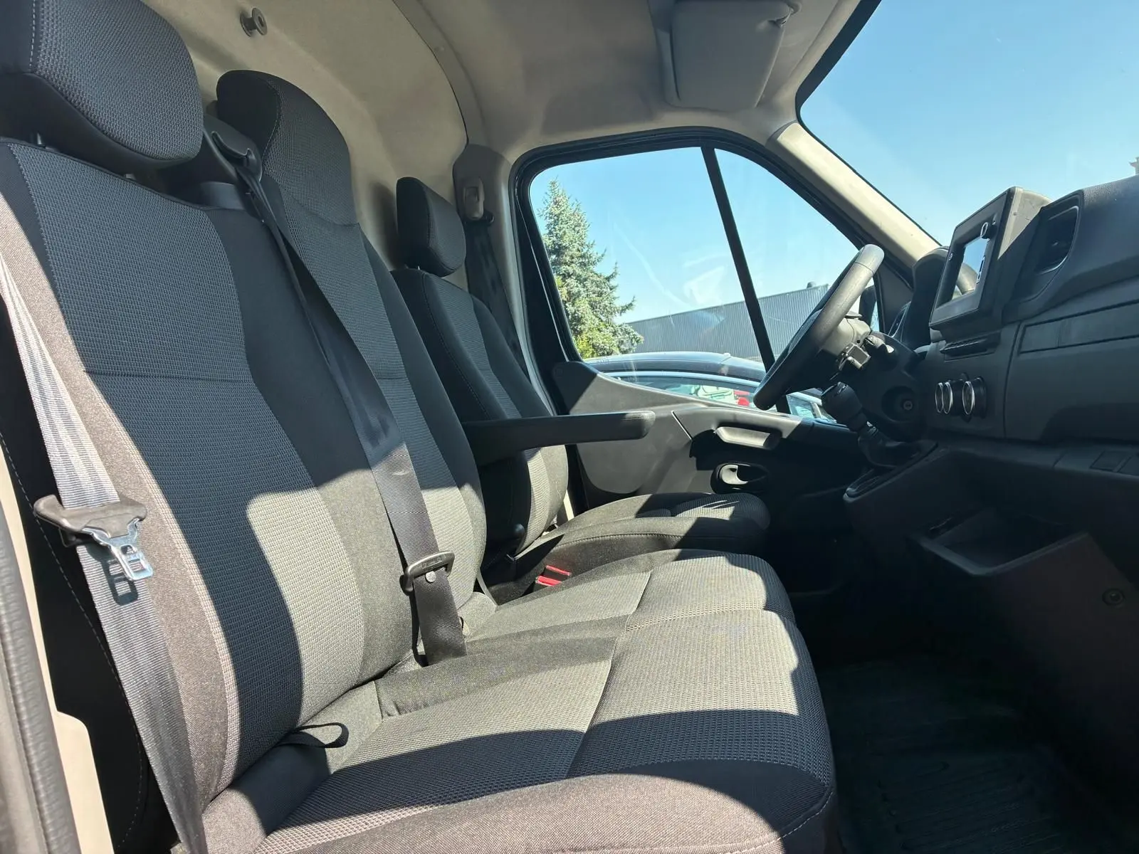 Vue intérieure côté conducteur du Renault Master gris 2023, montrant les sièges tissu gris et le tableau de bord avec écran tactile.