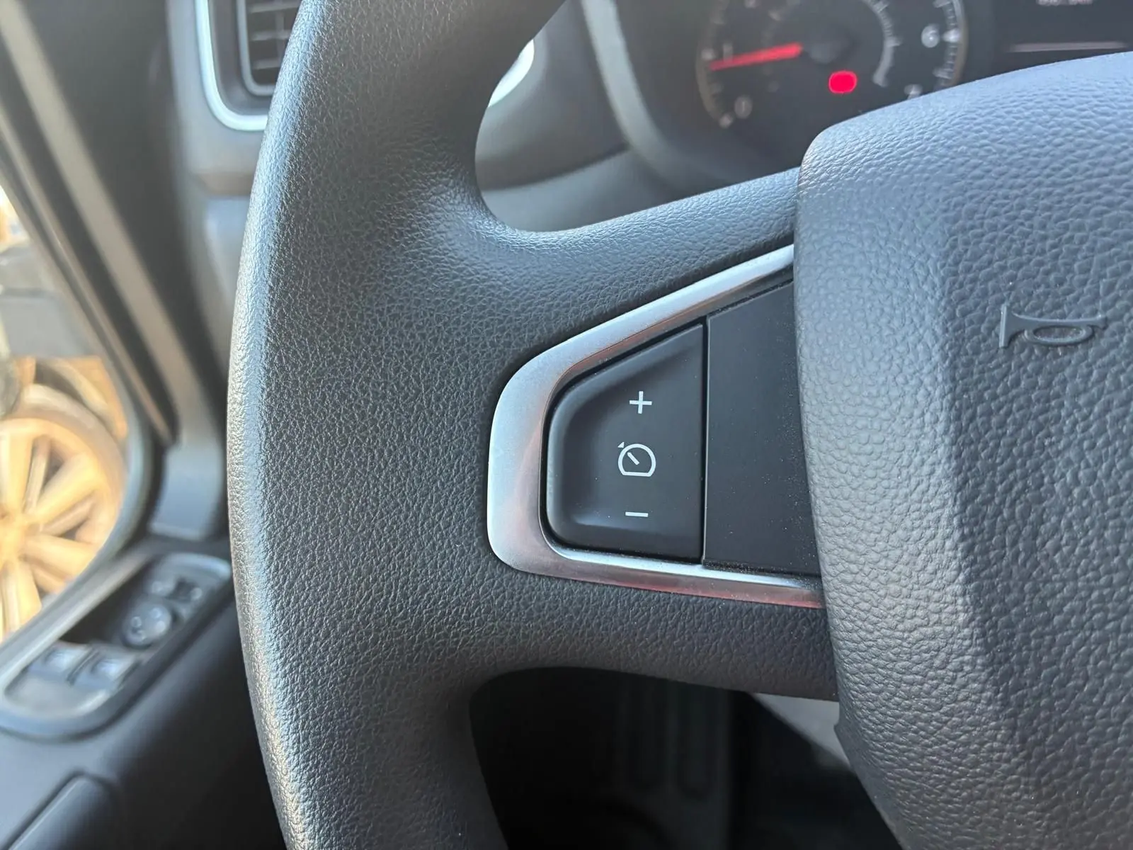 Gros plan sur le bouton de régulateur de vitesse au volant noir du Renault Master gris, vue intérieure côté conducteur.