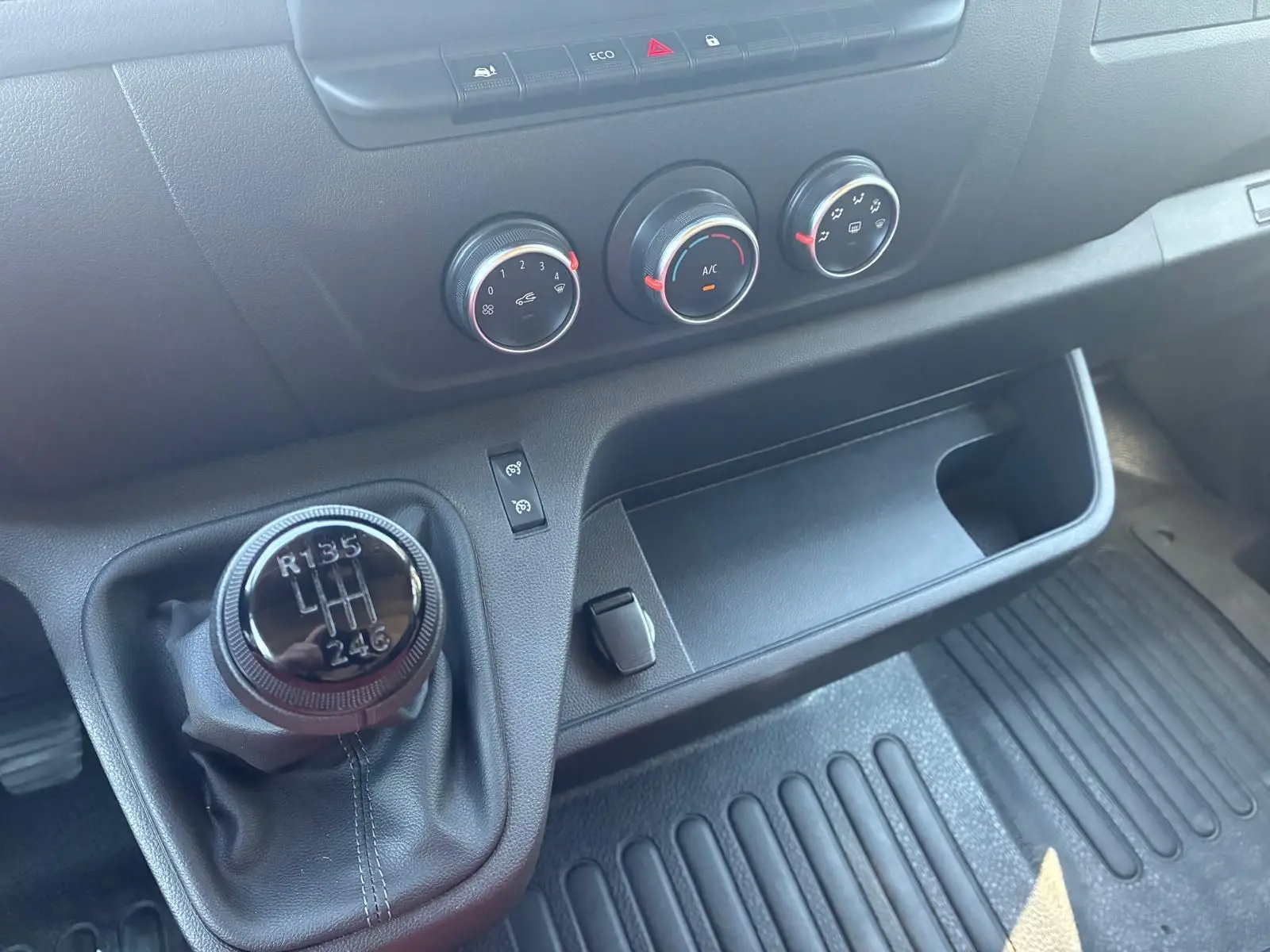 Gros plan sur la console centrale du Renault Master gris 2023, mettant en valeur le levier de vitesses manuel et les commandes de climatisation.