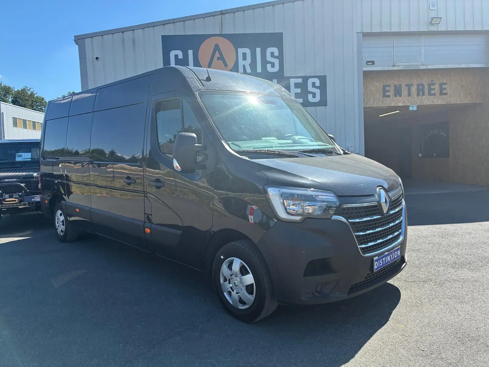 Renault Master gris 3/4 avant droit, grand utilitaire avec calandre chromée et jantes acier, stationné devant un bâtiment.