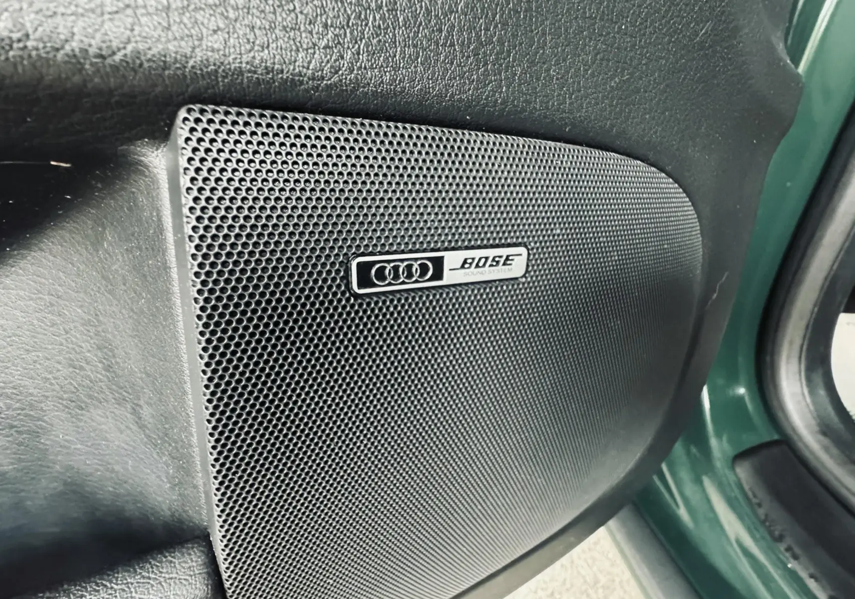 Gros plan sur l'enceinte Bose intégrée dans la porte côté gauche d'une Audi S4 Avant verte de 2004.