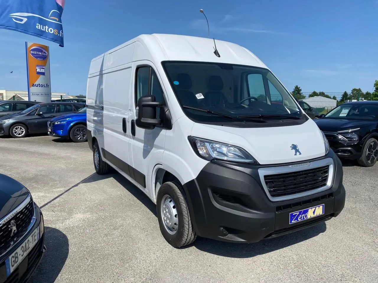 Vue 3/4 avant d'un Peugeot Boxer Fourgon blanc 2023 avec pare-chocs noirs et porte latérale droite coulissante.