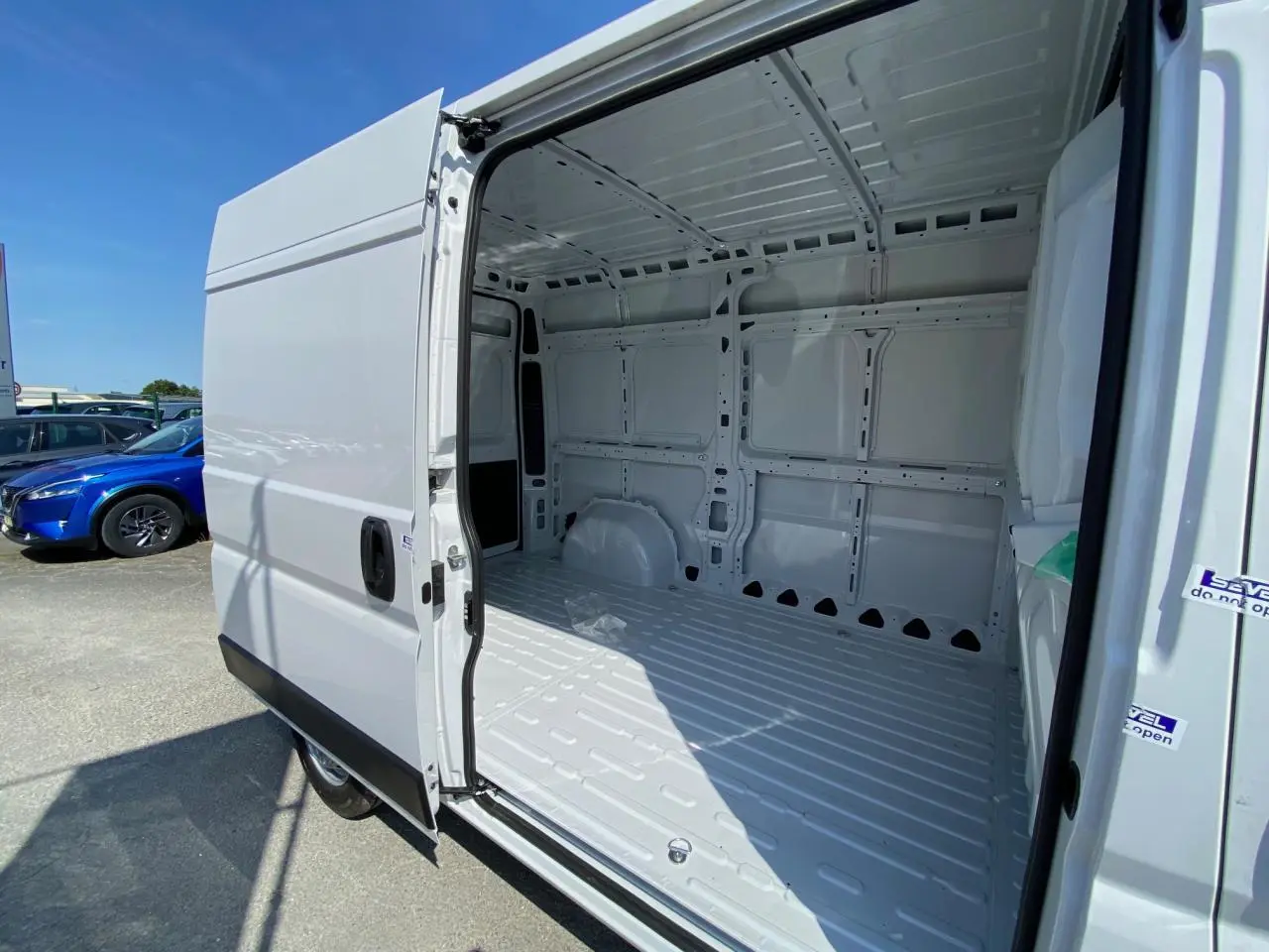 Vue latérale gauche du Peugeot Boxer Fourgon blanc 2023 avec porte coulissante ouverte montrant l'intérieur vide et tôlé.