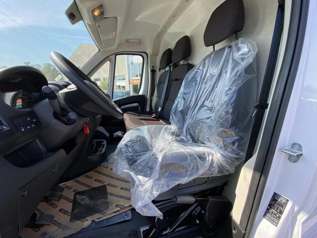 Vue intérieure côté conducteur du Peugeot Boxer Fourgon blanc 2023, sièges avant dont un protégé par un film plastique.