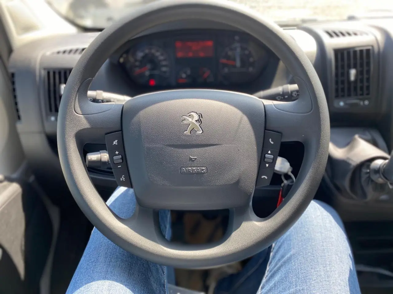 Vue intérieure centrée sur le volant Peugeot du Boxer Fourgon 2023, avec commandes intégrées et tableau de bord flou.